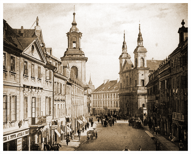 Ulica Freta w Warszawie. Fot. Maurycy Pusch, ok. 1895. Ze zbiorów Muzeum Narodowego w Warszawie
Warszawa. Ulica Freta. Widok w kierunku ulicy Nowomiejskiej, w głębi po prawej fasada kościoła pw. św. Ducha, po lewej wieża kościoła pw. św. Jacka. Pierwszy budynek od lewej, dwupiętrowy, z dwiema lukarnami i trójkątnym tympanonem z okrągłym oknem to kamienica pod numerem 16. Na pierwszym piętrze – balkon z ozdobną balustradą, na parterze – szyld apteki S. Tuguta w języku rosyjskim i polskim. Na chodniku przed wejściem stoi trzech mężczyzn i kobieta z parasolką. Na chodnikach i ulicy wielu przechodniów, na jezdni – szereg zaprzęgów konnych. Zdjęcie wykonano w słoneczny dzień.